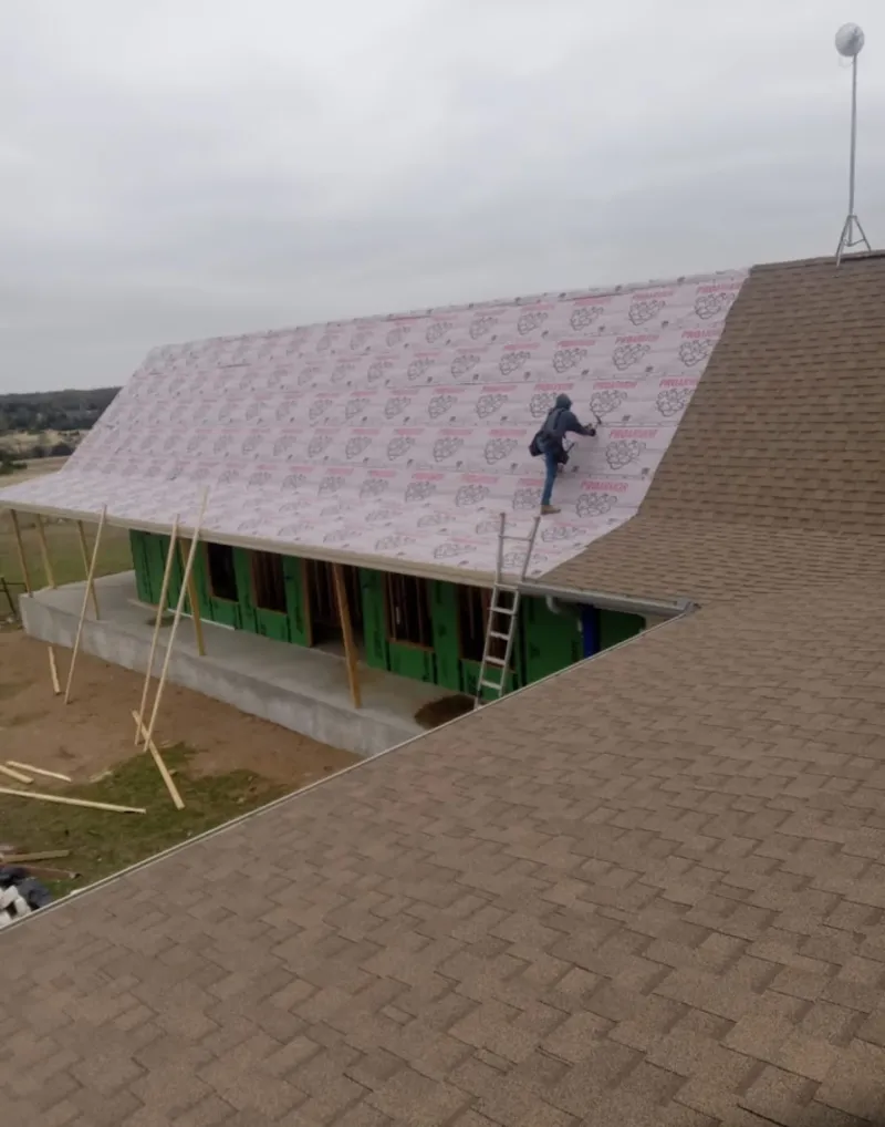 Worker preparing underlayment for a metal roof installation in Newfane